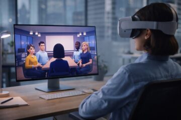 Persona in ufficio con visore VR che partecipa a una riunione virtuale nel metaverso mostrata sul monitor