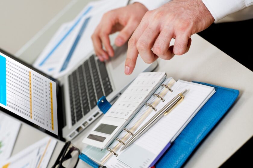 Persona che pianifica un investimento con laptop, documenti e taccuino su una scrivania