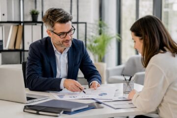 Consulente fiscale assiste un cliente in uno sportello CAF con documenti e laptop